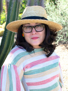 A photo of Diana Delgado, Executive Director of Hugo House. She is facing the camera, wearing a hat with a striped shirt.