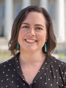 A headshot of Susan Evans McClure, Executive Director of Vermont Arts Council. She is smiling at the camera, wearing a dark, polka-dotted top and blue earrings.