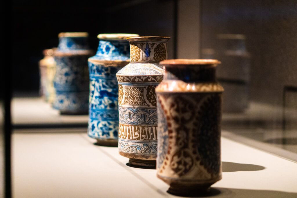 Three museum artifact vases lined in a row each with intricate and colorful designs.